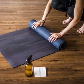 Woman rolling up yoga mat with sanitizer nearby.