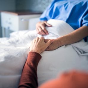 Woman holding hand of sister in hospital bed