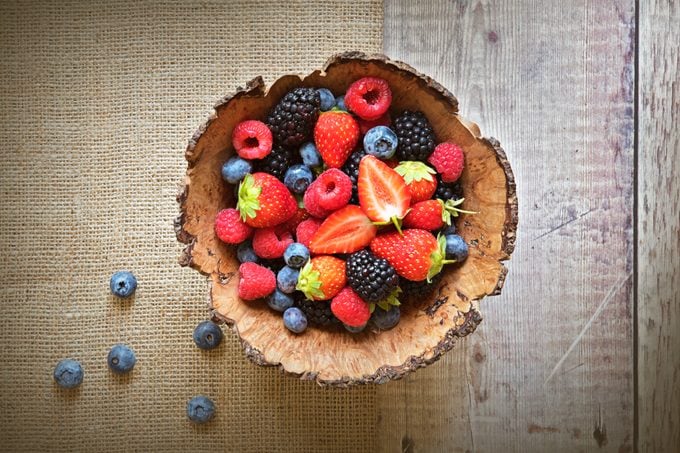 Close-up image of a wooden bowl full of Healthy Summer berries including Strawberries, raspberries, black berries and blue berries