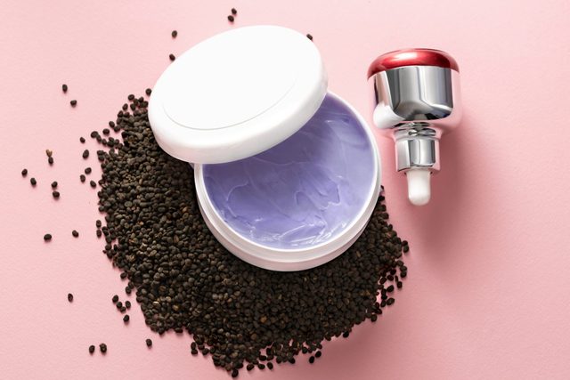 Babchi dry raw seeds (Psoralea Corylifolia) on pink surface with various kinds of cosmetic products. Bakuchiol cosmetics concept.