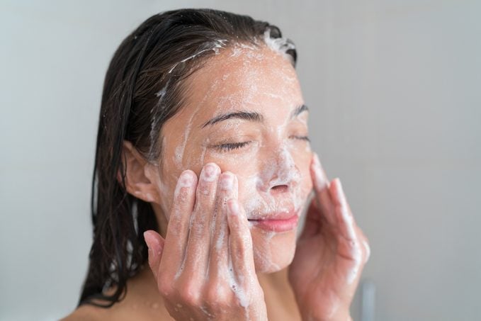 Donna per la cura della pelle che si lava il viso sotto la doccia
