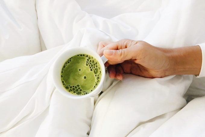 High Angle View Of Woman Holding Matcha Latte In A Mug In Bed