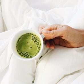 High Angle View Of Woman Holding Matcha Latte In A Mug In Bed