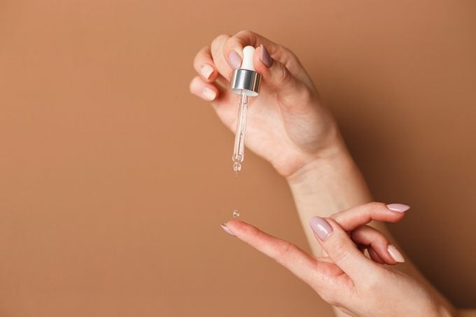 Hands of cropped white woman holding cosmetic serum pipette on the orange background