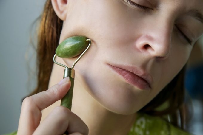 Mujer usando un rodillo facial de jade para el cuidado de la piel.