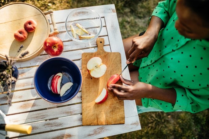 Woman Cutting Fruit Outdoors Preparing Snack For Family