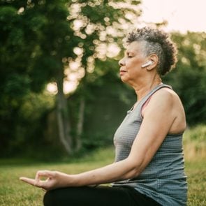Side view of senior woman with in-ear headphones sitting in lotus position at park