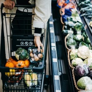 Close up of woman's hand shopping for fresh groceries in supermarket and putting a variety of organic vegetables in shopping cart