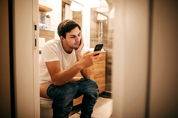 man sitting on toilet and looking at smartphone