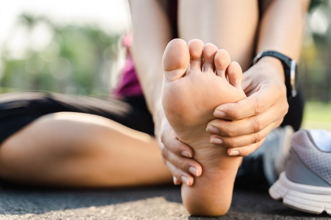 Low Section Of Woman Touching Foot In Pain While Sitting On Road
