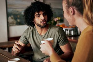 Young African American man with an afro in serious conversation with woman while sitting in a cafe and drinking coffee - two diverse friends chatting in a coffee shop