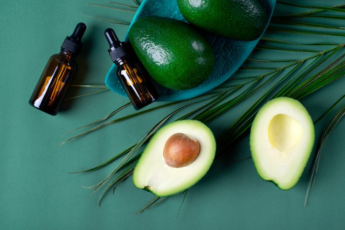 Avocado oil in dropper bottle and avocados on the green background