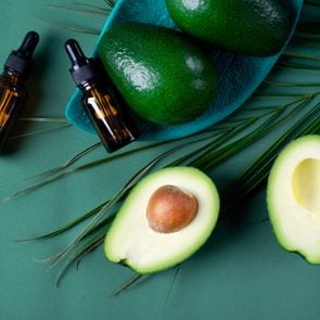 Avocado oil in dropper bottle and avocados on the green background
