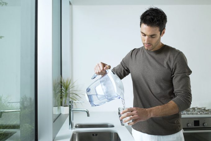 Man in kitchen pouring glass of filtered water