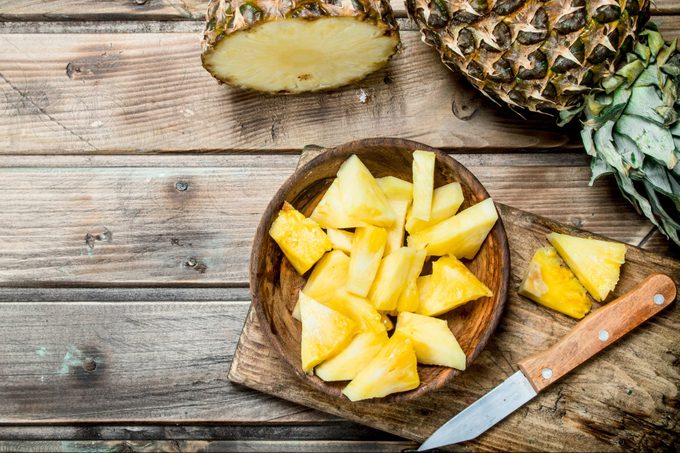 Pieces of fragrant pineapple in a bowl on a cutting Board with a knife.