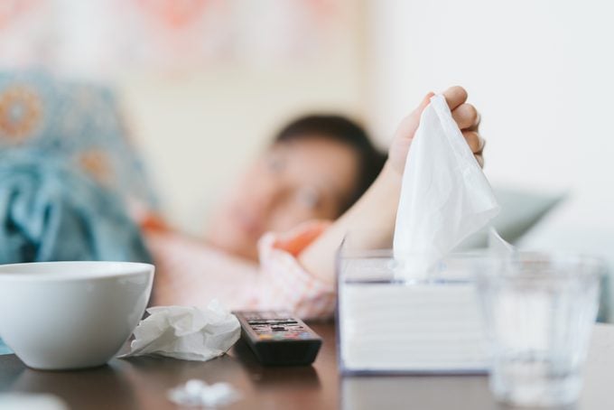Woman feeling sick at home blowing her nose with tissue papers