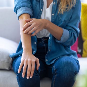 Young woman scratching her arm while sitting on the sofa at home.