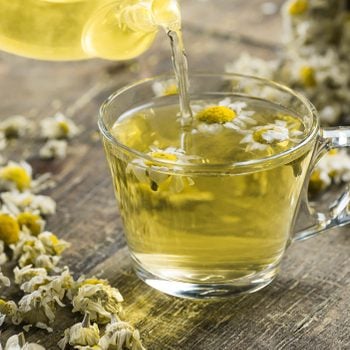 glass cup of chamomile tea with dry daisy flowers and teapot on rustic wooden background, herbal medicine hot drink concept