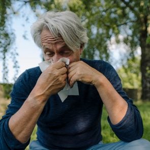man blowing nose while sitting in field