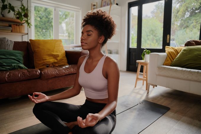 Young black woman doing yoga at home in the lotus position