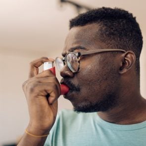 Headshot of a young African American man using asthma inhaler