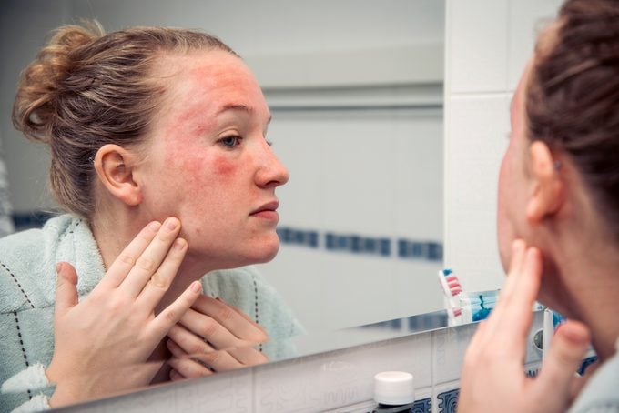 woman looking at skin reaction on face in bathroom mirror