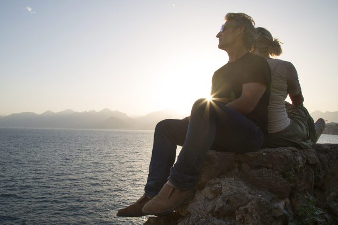 Couple sit on rock above sea, looking off