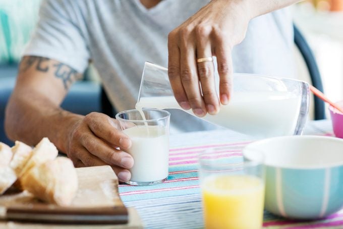 Midsection of man pouring milk in drinking glass at table