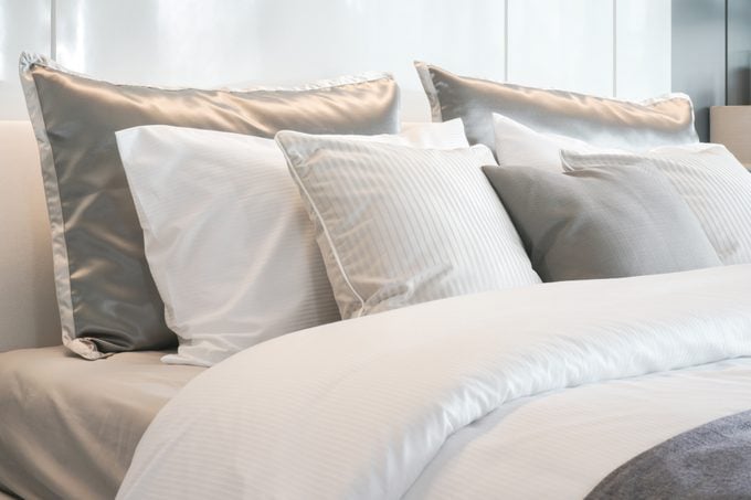 Graue Farbschema-Kissen, die auf dem Bett liegen, mit Bettwäsche im Satin-Stil