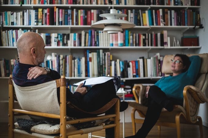 Male therapist discussing with female mature patient against bookshelf at home office