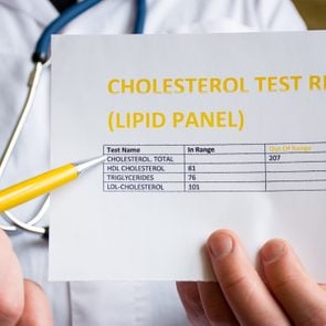Doctor indicates patient or colleague on cholesterol test result or lipid panel, standing in white medical coat. Concept photo to illustrate diagnostic and screening of high or low blood cholesterol