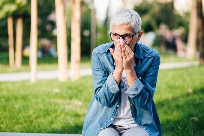 woman in park sneezing into a tissue