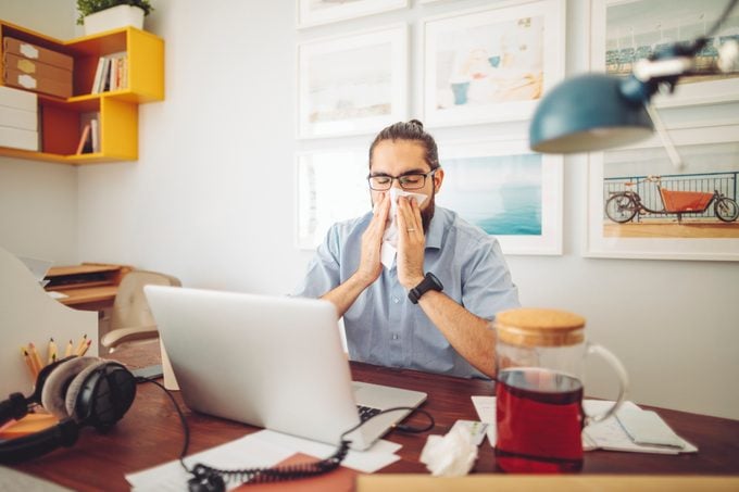 man suffering from allergies while working from home