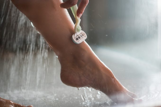 Primo piano di una donna irriconoscibile che si rade la gamba nell'acqua della doccia