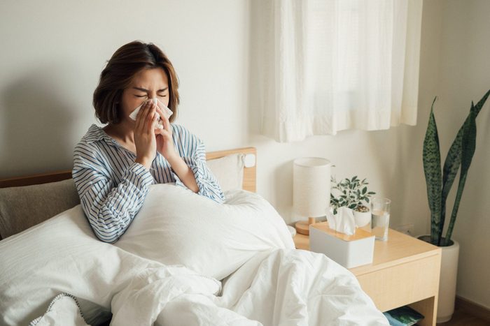 young woman with allergies in bed blowing her nose into a tissue