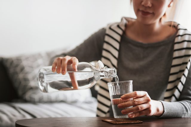 close up of young woman pouring herself a glass of water at home