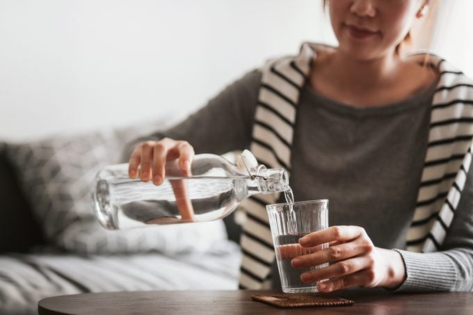 close up of young woman pouring herself a glass of water at home