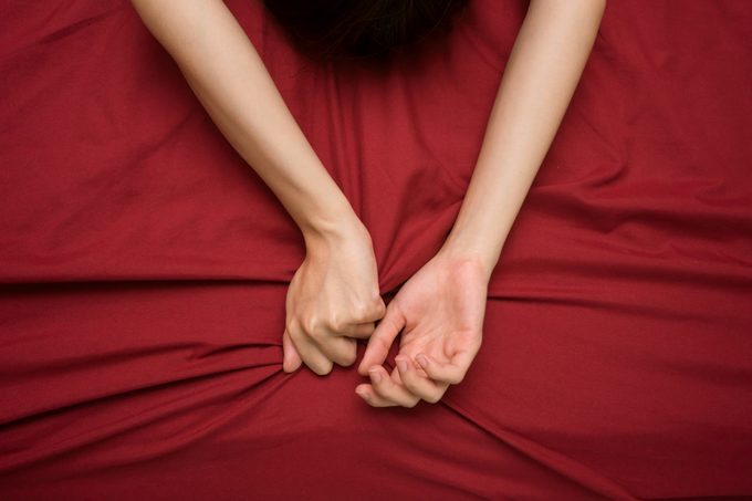 woman's hands on maroon colored bed sheets