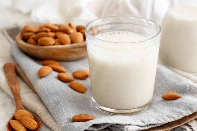 glass of almond milk surrounded but almonds