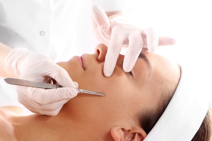 dermatologist dermaplaning woman's face with scalpel object