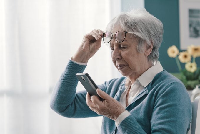 Senior woman having vision problems while looking at smartphone