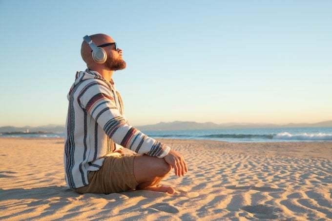 Man with headphones on meditating at the beach