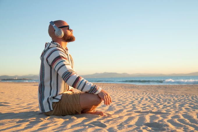 Uomo con le cuffie che medita sulla spiaggia