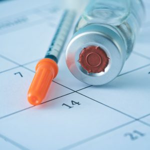 Syringe and Vaccine on top of a Calendar