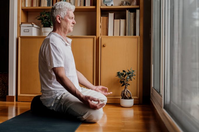Man practicing meditation while sitting in lotus position at home