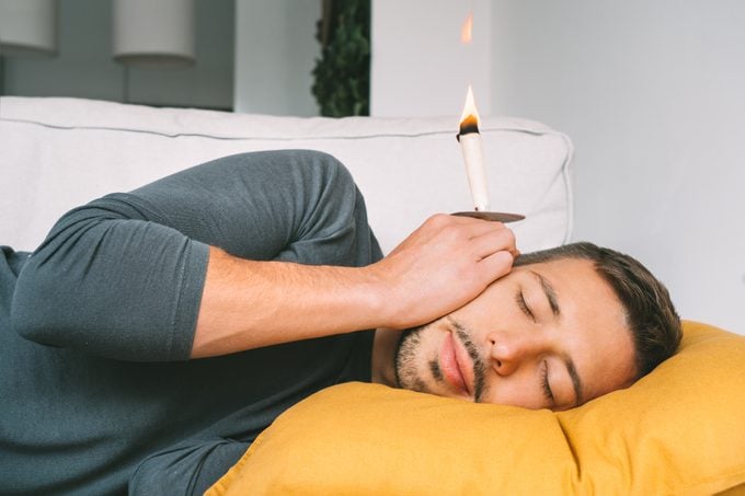 Man using ear candle for ear wax treatment at home on the couch