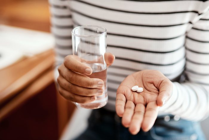 close up of woman holding two pills in one hand and a glass of water in the other