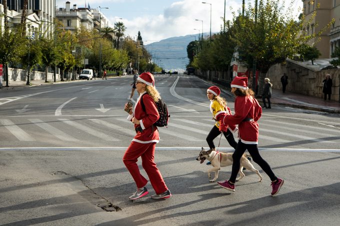 People dressed as Santa Claus running with their dog