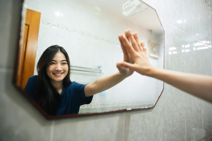 young woman smiling in mirror and giving herself a high five