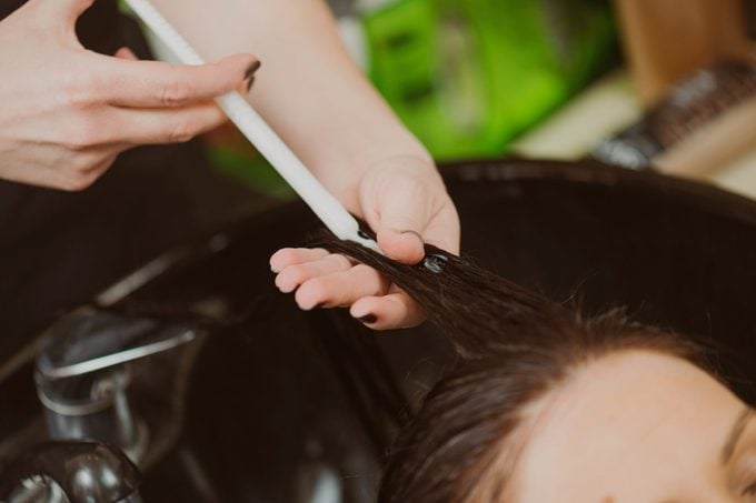 primo piano del parrucchiere che applica il botox per capelli ai capelli del cliente